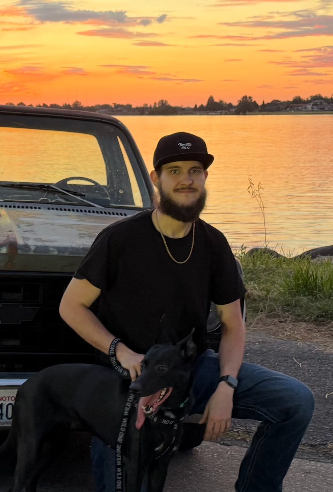 Jakob Knight kneeling beside his dog in front of a pickup at sunset