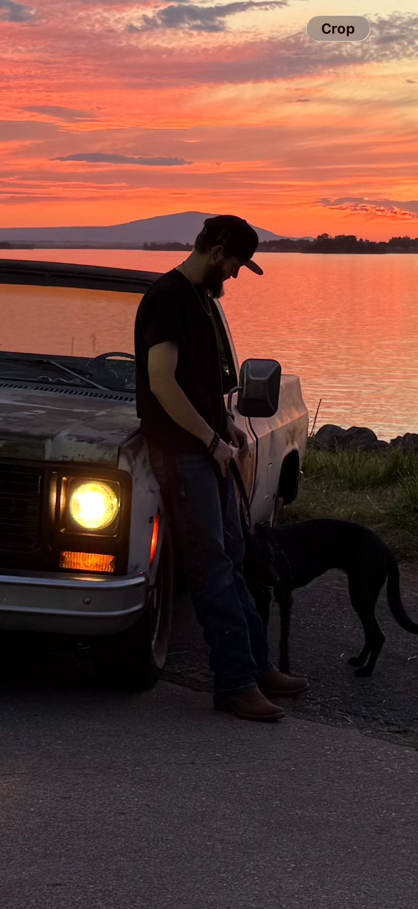 Jakob standing by an old pickup with the headlights on at sunset
